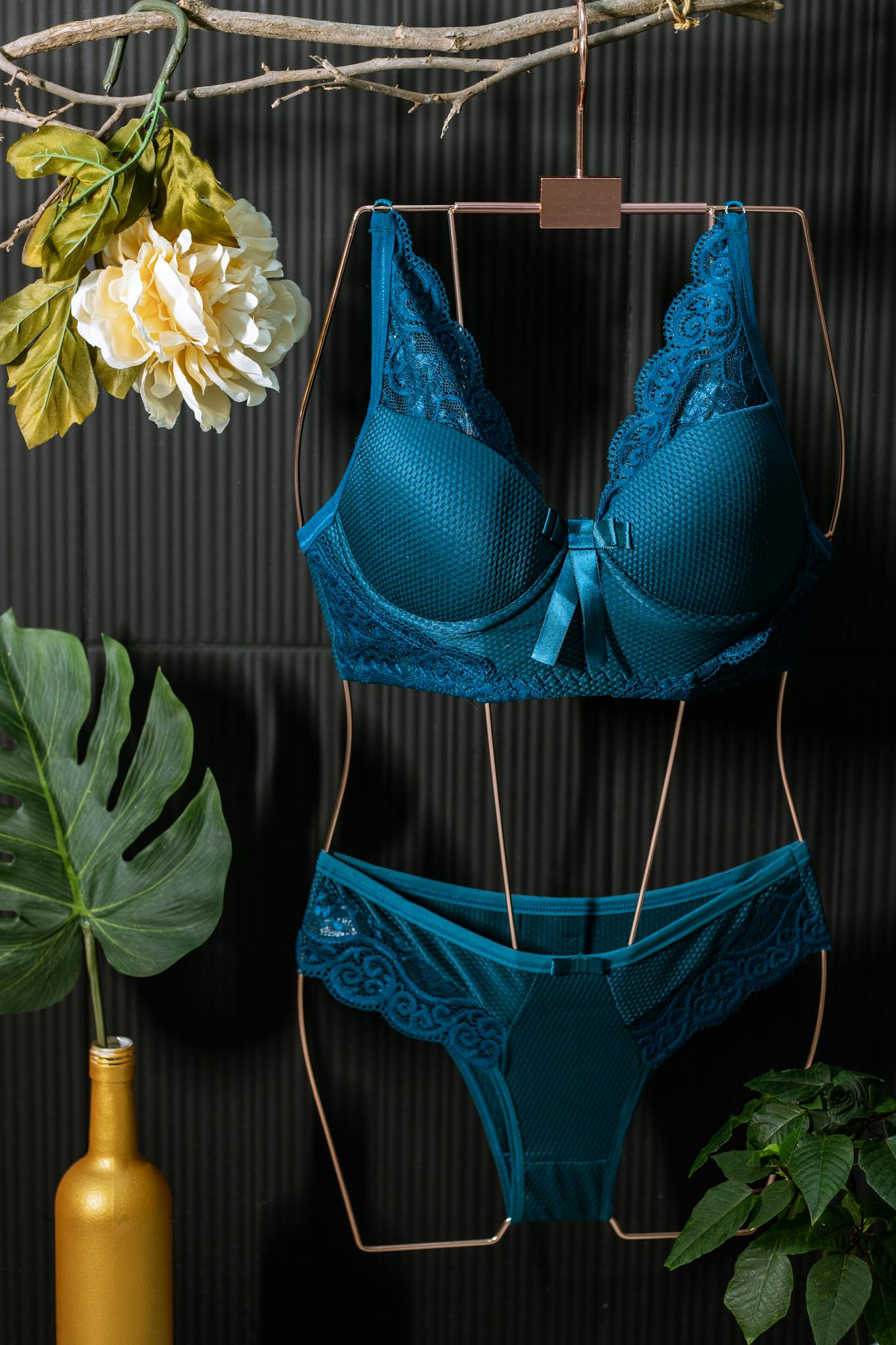 Blue lingerie set on hanger with decorative leaves and flowers against dark background.